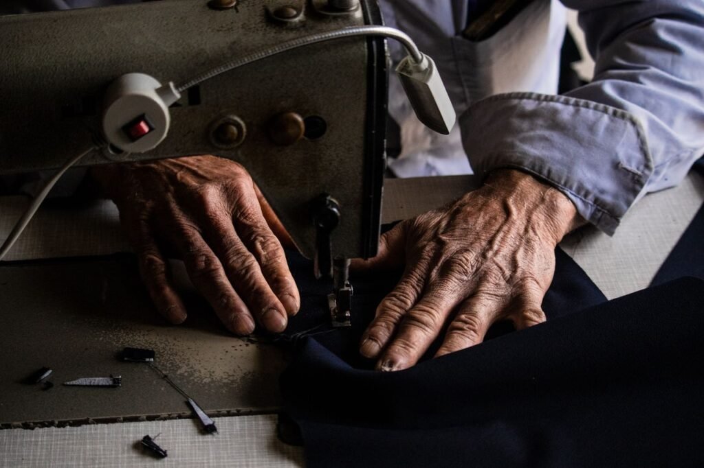 An elderly tailor working indoors, skillfully using a sewing machine.