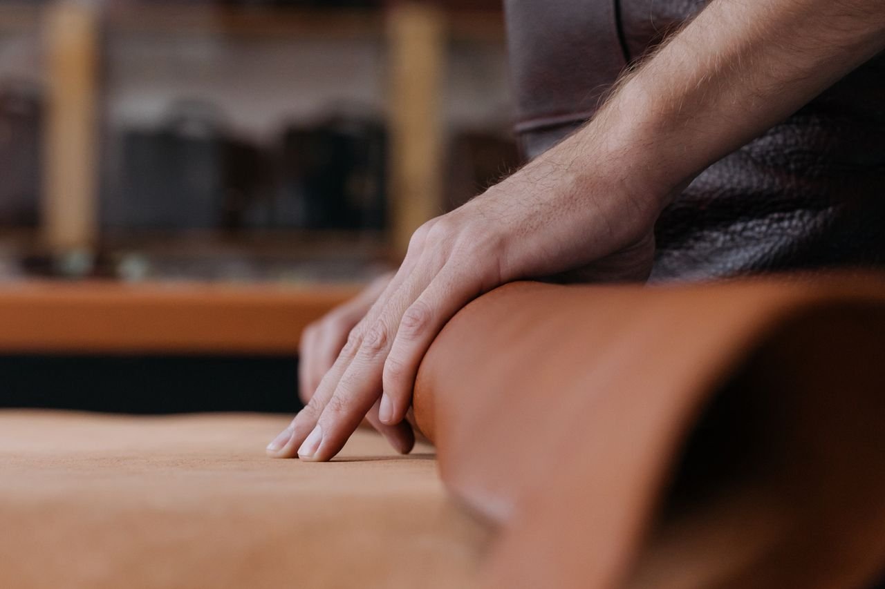 Close-up of hands working with leather in a workshop, emphasizing craftsmanship and detail.