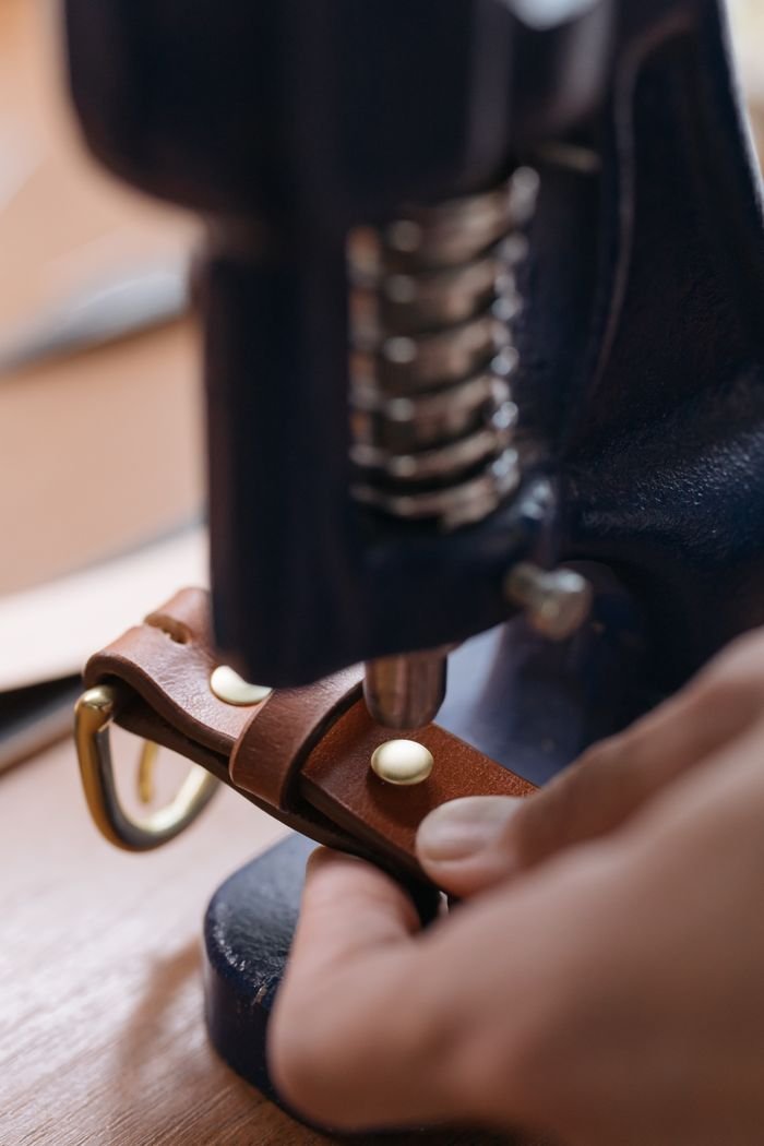 Detailed view of crafting a leather belt using a press machine, showcasing craftsmanship.